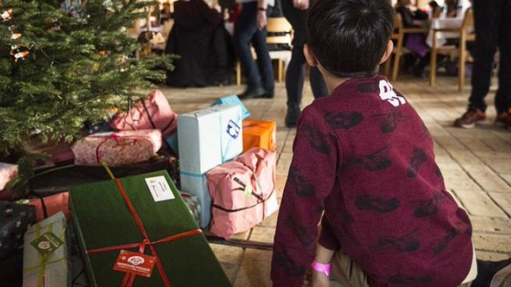 Et barn og gaver ved juletræet. En gave er markeret med Børnehjælpsdagens logo.